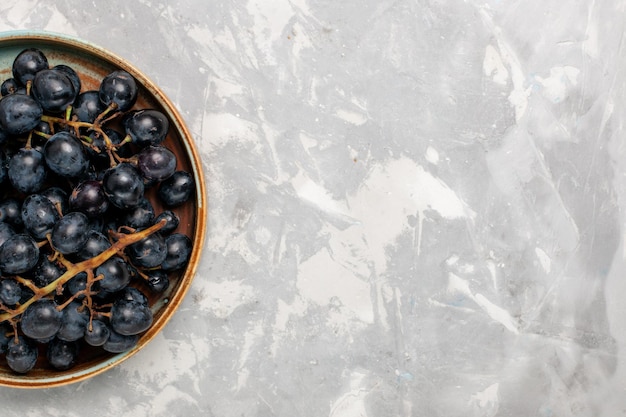 Vue de dessus raisins noirs frais juteux fruits sucrés moelleux sur le bureau blanc clair