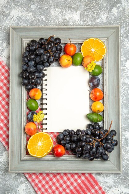 Vue de dessus des raisins noirs frais avec des oranges et du feijoa à l'intérieur du cadre sur une surface blanche fruits mûrs moelleux frais