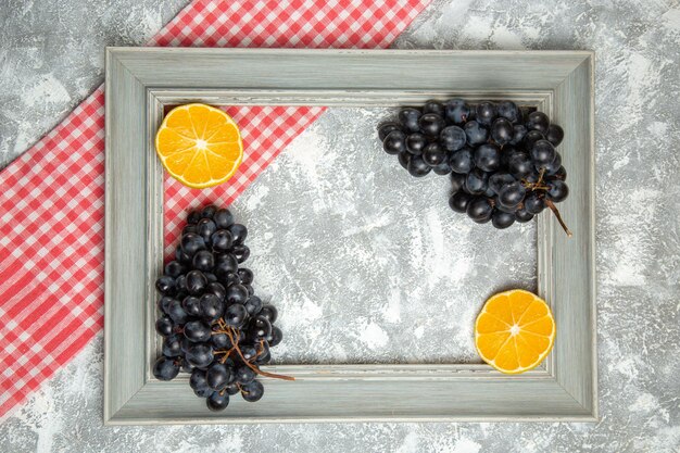 Vue de dessus des raisins noirs frais avec des oranges à l'intérieur du cadre sur une surface blanche fruits mûrs moelleux frais