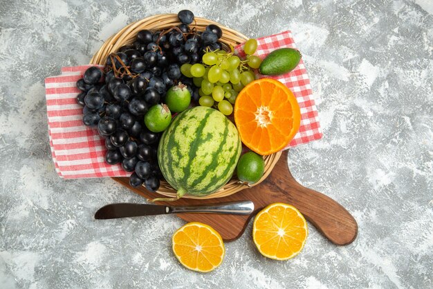 Vue de dessus des raisins noirs frais avec des oranges et de la pastèque sur une surface blanche, des fruits mûrs, des vitamines douces, des arbres frais