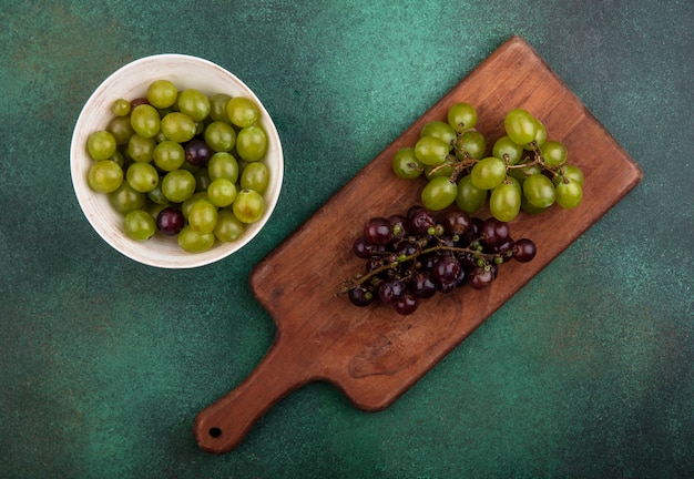 Vue de dessus des raisins sur une planche à découper avec des baies de raisin dans un bol sur fond vert