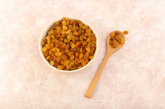 Une vue de dessus les raisins secs orange à l'intérieur de la plaque ronde blanche avec une cuillère en bois sur rose