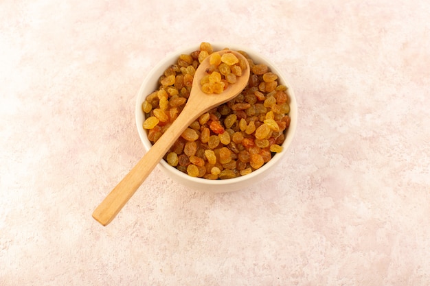 Une vue de dessus les raisins secs orange à l'intérieur de la plaque ronde blanche avec une cuillère en bois sur rose