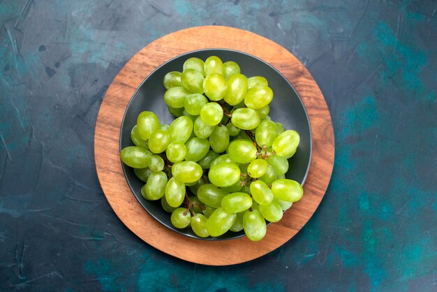 Vue de dessus des raisins verts frais moelleux fruits juteux à l'intérieur de la plaque sur le bureau bleu foncé.