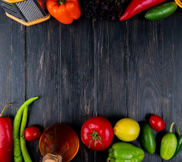 Vue de dessus de la râpe et une bouteille d'huile d'olive avec des légumes frais piments verts tomates concombres poivrons colorés et citron sur bois foncé avec espace de copie