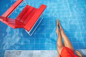 Photo gratuite vue de dessus recadrée de pieds de femme sexy trempant dans la piscine jolies jambes féminines en bikini profitant de l'eau fraîche au bord de la piscine s'asseoir sur le bord de la piscine près de la chaise de sauveteur rouge concept de voyage et de tourisme