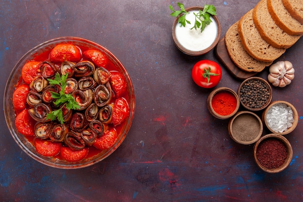 Vue de dessus repas de légumes cuits tomates et aubergines avec assaisonnements et pain sur un bureau sombre