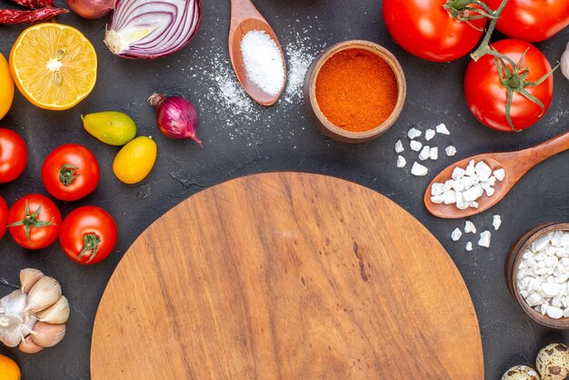 Vue de dessus ronde planche de bois sel dans des cuillères en bois ail cumcuats tomates citron sur table sombre