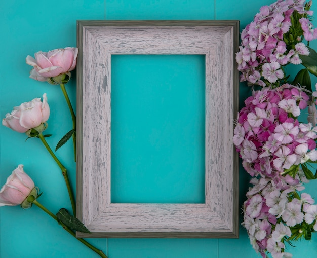 Vue de dessus des roses rose clair avec cadre gris et fleurs violet clair sur une surface bleu clair