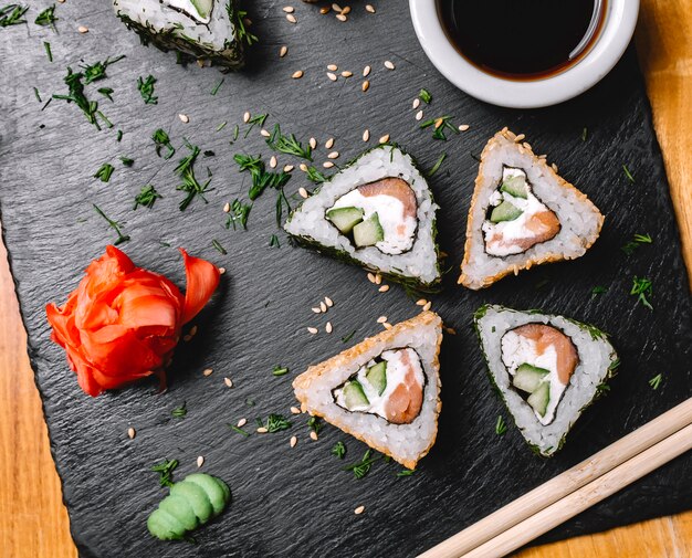 Vue de dessus rouleau de sushi au saumon, fromage à la crème, concombre wasabi, gingembre et sauce soja sur une planche