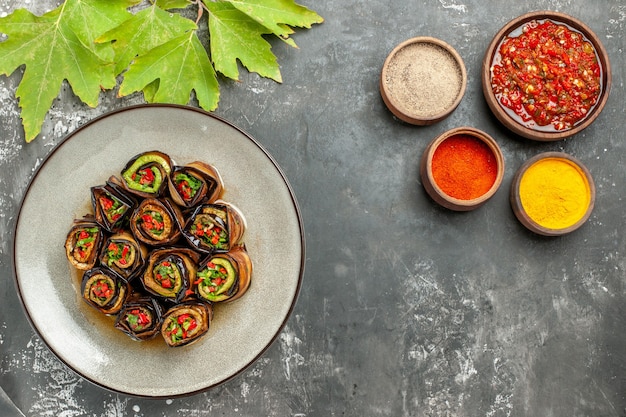 Vue de dessus des rouleaux d'aubergines farcies dans une assiette blanche adjika de curcuma en poudre de piment sur fond gris espace libre