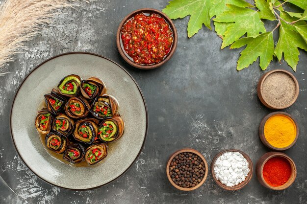 Vue de dessus des rouleaux d'aubergines farcies différentes épices adjika dans de petits bols sur fond gris