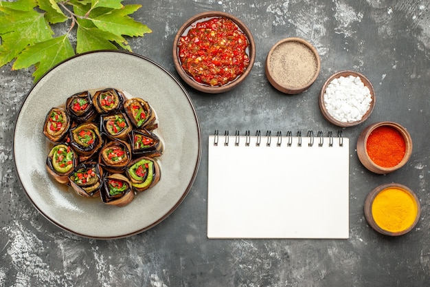 Vue de dessus rouleaux d'aubergines farcies épices dans de petits bols sel poivre poivre rouge curcuma adjika un cahier sur une surface grise