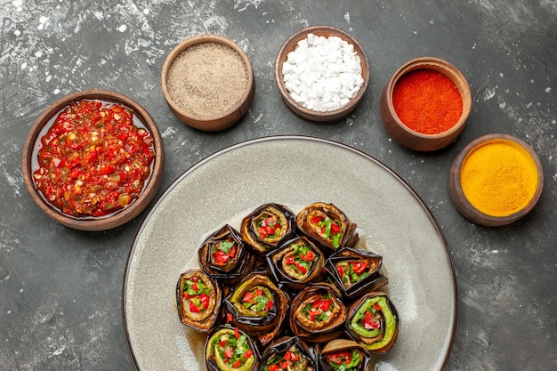 Vue de dessus rouleaux d'aubergines farcies épices dans de petits bols sel poivre rouge curcuma adjika sur surface grise