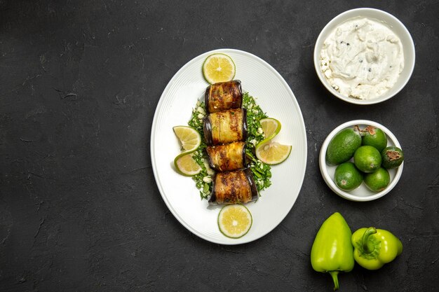 Vue de dessus des rouleaux d'aubergines salés plat cuit avec des tranches de citron et du feijoa sur la surface sombre du dîner à l'huile plat de cuisson des aliments