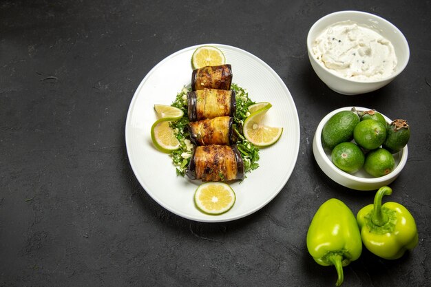 Vue de dessus des rouleaux d'aubergines salés plat cuit avec des tranches de citron et du feijoa sur une surface sombre plat de repas de cuisson à l'huile