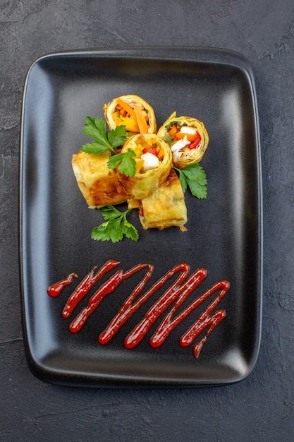 Vue de dessus des rouleaux de pâté de légumes à l'intérieur de la plaque noire sur une surface sombre