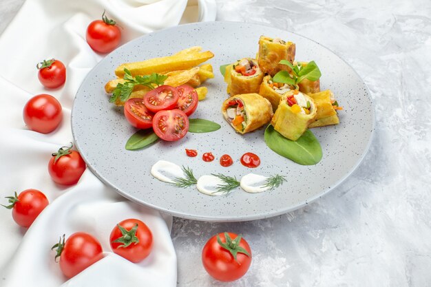 Vue de dessus des rouleaux de pâté de légumes avec des tomates et des frites à l'intérieur de la plaque sur une surface blanche