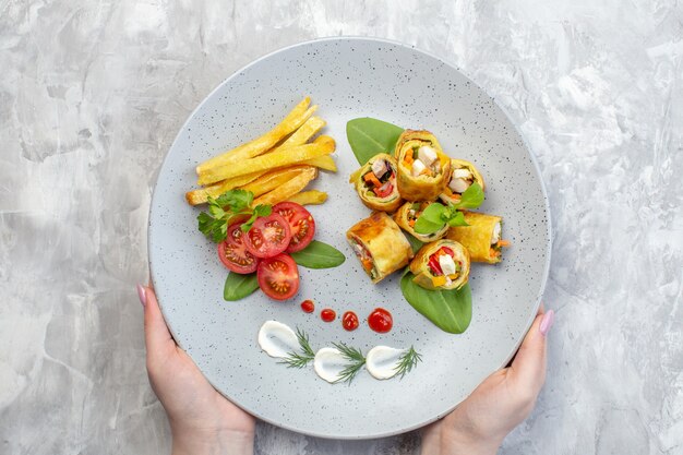 Vue de dessus des rouleaux de pâté de légumes avec des tomates et des frites à l'intérieur de la plaque sur une surface blanche