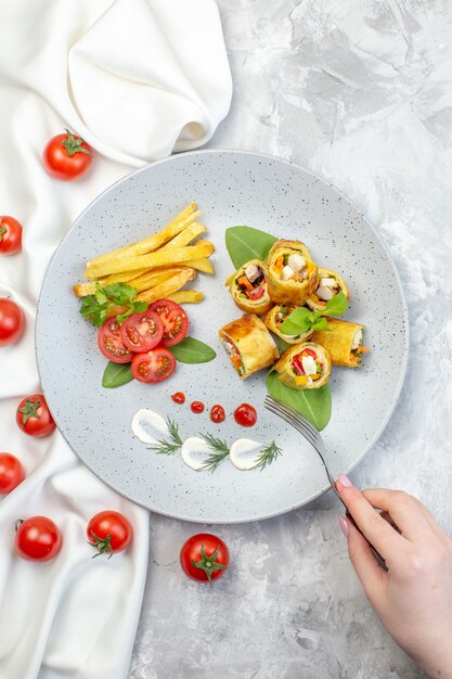 Vue de dessus des rouleaux de pâté de légumes avec des tomates et des frites à l'intérieur de la plaque sur une surface blanche