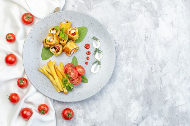 Vue de dessus des rouleaux de pâté de légumes avec des tomates et des frites à l'intérieur de la plaque sur une surface blanche