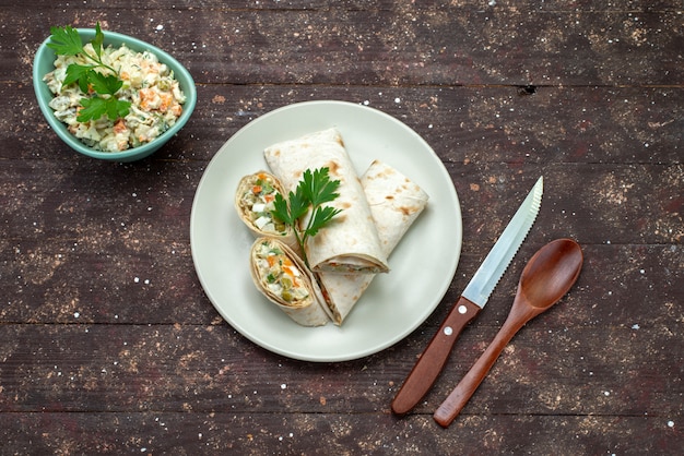 Vue de dessus des rouleaux de sandwich en tranches avec de la salade et de la viande à l'intérieur avec une assiette blanche de salade mayyonaise sur le bureau en bois brun snack-repas repas sandwich