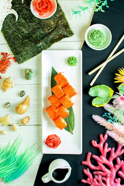 Vue de dessus de rouleaux de sushi avec du fromage à la crème de chair de crabe et de l'avocat dans du caviar de poisson volant avec de la sauce de soja sur une feuille de bambou