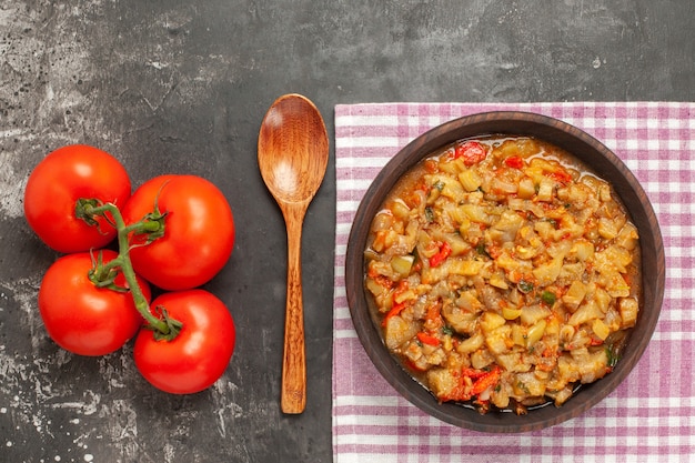 Photo gratuite vue de dessus de la salade d'aubergines rôties dans un bol, cuillère en bois et tomates sur une surface sombre