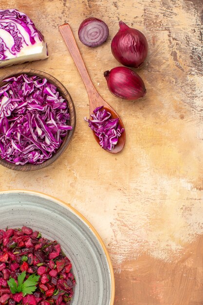 Vue de dessus de la salade de betteraves saines dans une assiette grise faite d'oignons rouges et d'un bol de chou rouge haché et sur un fond en bois avec place pour copie