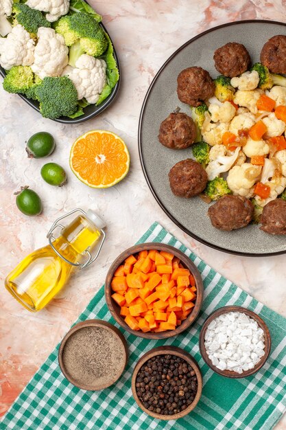 Vue de dessus salade de brocoli et chou-fleur et boulette de viande sur assiette serviette à carreaux vert et blanc huile crudités sur assiette tranche de citron feykhoas différentes épices dans de petits bols sur fond nu