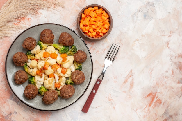 Vue de dessus de la salade de brocoli et de chou-fleur et boulette de viande sur un bol en assiette avec une carotte coupée une fourchette sur fond nu avec espace de copie