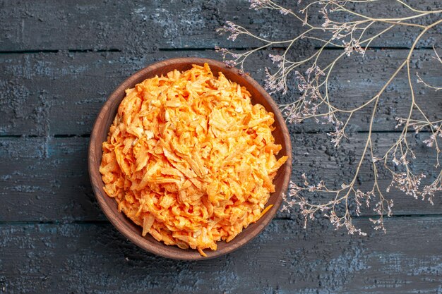 Vue de dessus de la salade de carottes râpées à l'intérieur d'une assiette brune sur le bureau rustique bleu foncé salade de santé couleur légume de régime mûr