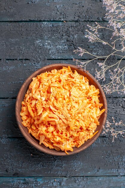 Vue de dessus de la salade de carottes râpées à l'intérieur d'une assiette brune sur le bureau rustique bleu foncé salade de santé couleur légume de régime mûr