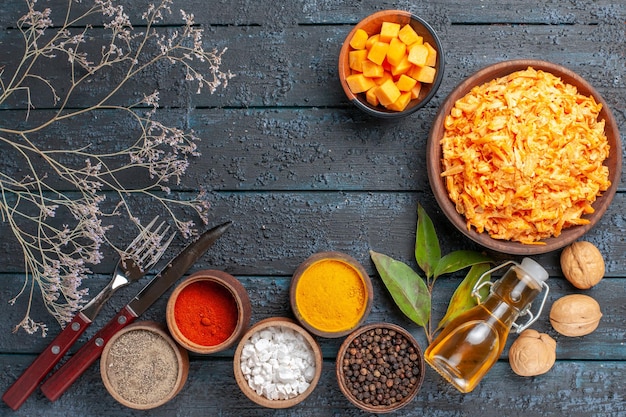 Vue de dessus de la salade de carottes râpées avec des noix à l'ail et des assaisonnements sur un bureau rustique bleu foncé régime végétal de santé couleur de salade mûre