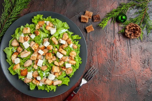 Vue de dessus de la salade césar sur une assiette ovale croûte séchée à la fourchette sur une table rouge foncé