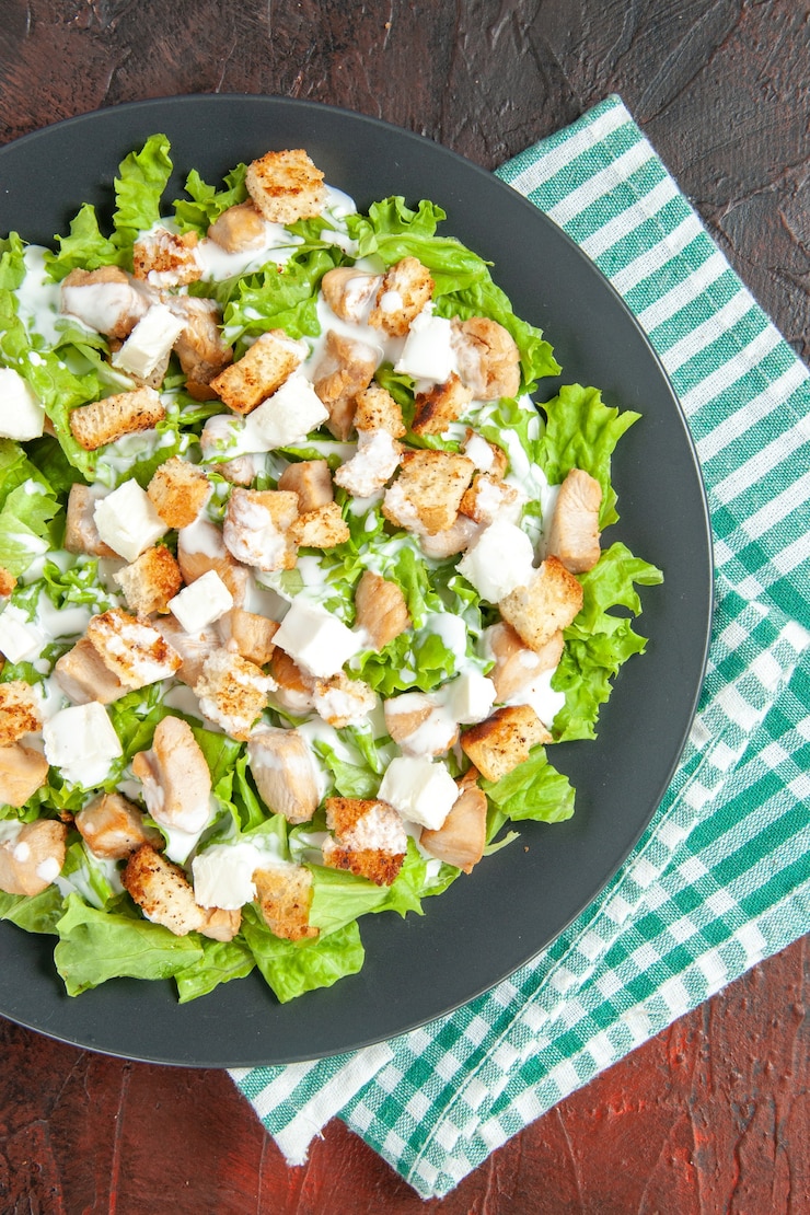 Photo gratuit vue de dessus de la salade césar sur une assiette ovale nappe à carreaux blanc vert sur fond rouge foncé