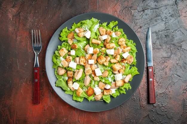 Photo gratuite vue de dessus de la salade césar sur une fourchette et un couteau à assiette ovale sur fond rouge foncé