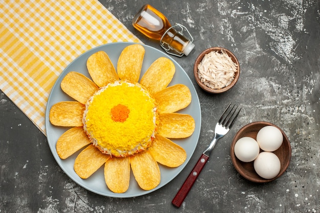 Vue de dessus de la salade sur le côté gauche avec une serviette jaune en dessous avec une bouteille d'huile de fourche à fromage et un bol d'oeufs sur le côté sur la table gris foncé