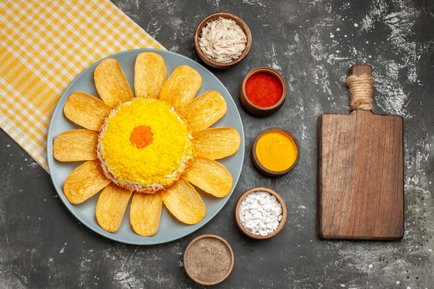 Vue de dessus de la salade sur le côté gauche avec une serviette jaune en dessous avec une planche à découper aux herbes sur le côté sur table gris foncé