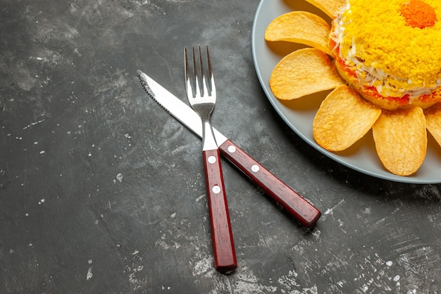 Photo gratuite vue de dessus de la salade sur le côté supérieur droit avec fourchette et couteau sillonné sur le côté sur fond noirâtre