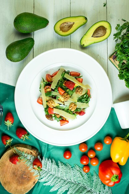 Vue de dessus de la salade fraîche au parmesan, avocat, noix, tomates cerises et fraises dans un bol blanc