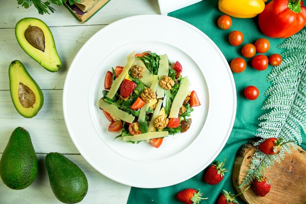 Vue de dessus de la salade fraîche au parmesan, avocat, noix, tomates cerises et fraises dans un bol blanc