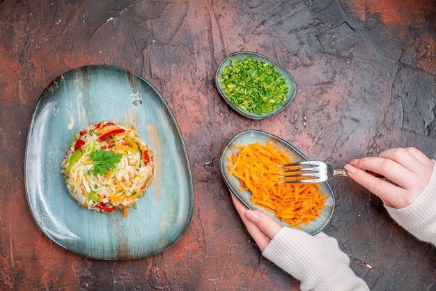 Vue de dessus de la salade de légumes frais à l'intérieur de l'assiette avec des carottes tranchées et des légumes verts sur une table sombre