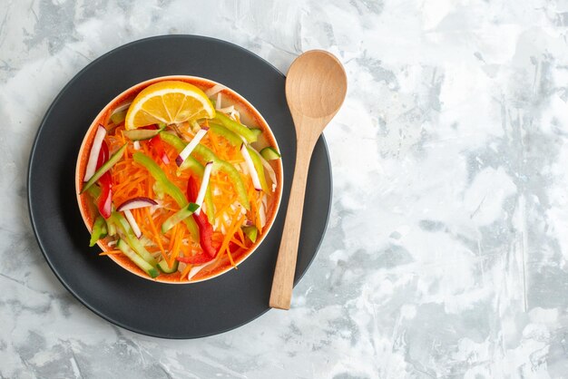 Vue de dessus salade de légumes frais à l'intérieur de la plaque avec une cuillère en bois sur une surface blanche nourriture repas régime dîner horizontal santé espace libre