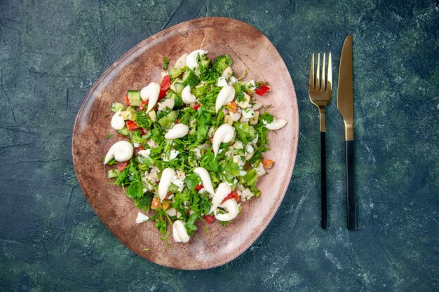 Vue de dessus salade de légumes frais à l'intérieur de la plaque élégante avec des couverts sur la surface bleu foncé santé déjeuner cuisine restaurant couleur repas régime