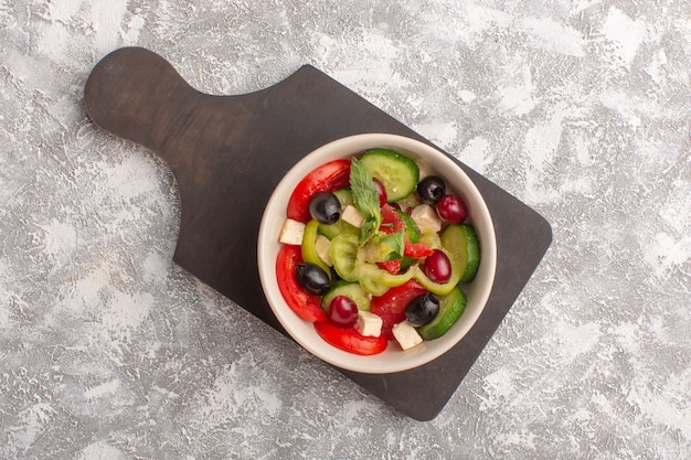 Vue de dessus salade de légumes frais avec des tranches de concombres tomates olive et fromage blanc à l'intérieur de la plaque sur le bureau gris repas de salade de légumes