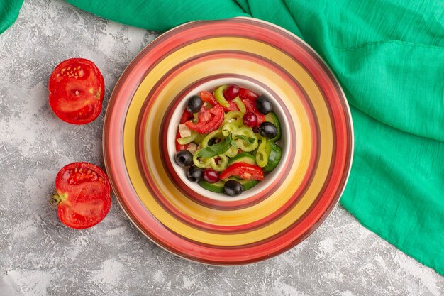 Vue de dessus salade de légumes frais avec des tranches de concombres tomates olive et fromage blanc à l'intérieur de la plaque sur la table grise salade de légumes collation repas