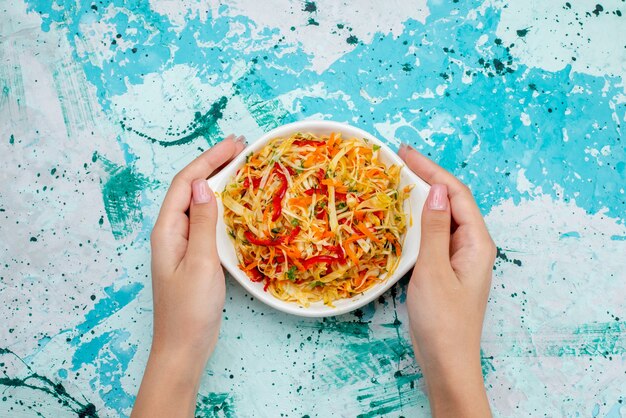 Vue de dessus salade de légumes frais en tranches de salade à l'intérieur de la plaque de maintien par femme sur la surface bleu vif repas salade de légumes collation