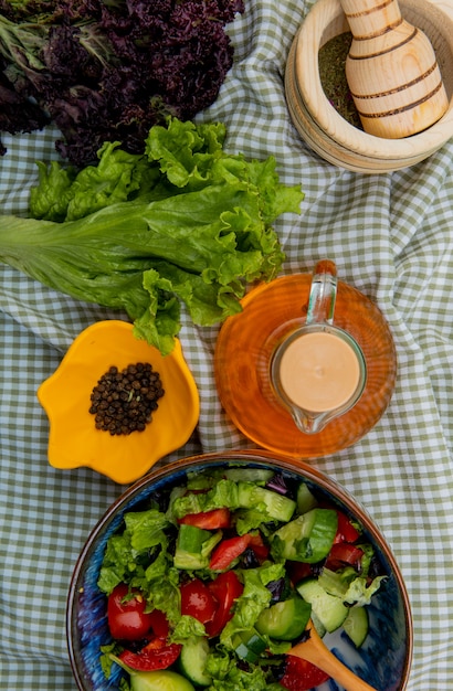 Photo gratuite vue de dessus de salade de légumes avec de la laitue basilic poivre noir concasseur d'ail beurre fondu sur la surface de tissu à carreaux