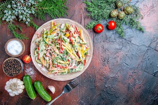 Vue de dessus salade de légumes sur plaque fourche tomates branches de pin concombres ail sur table rouge foncé place libre